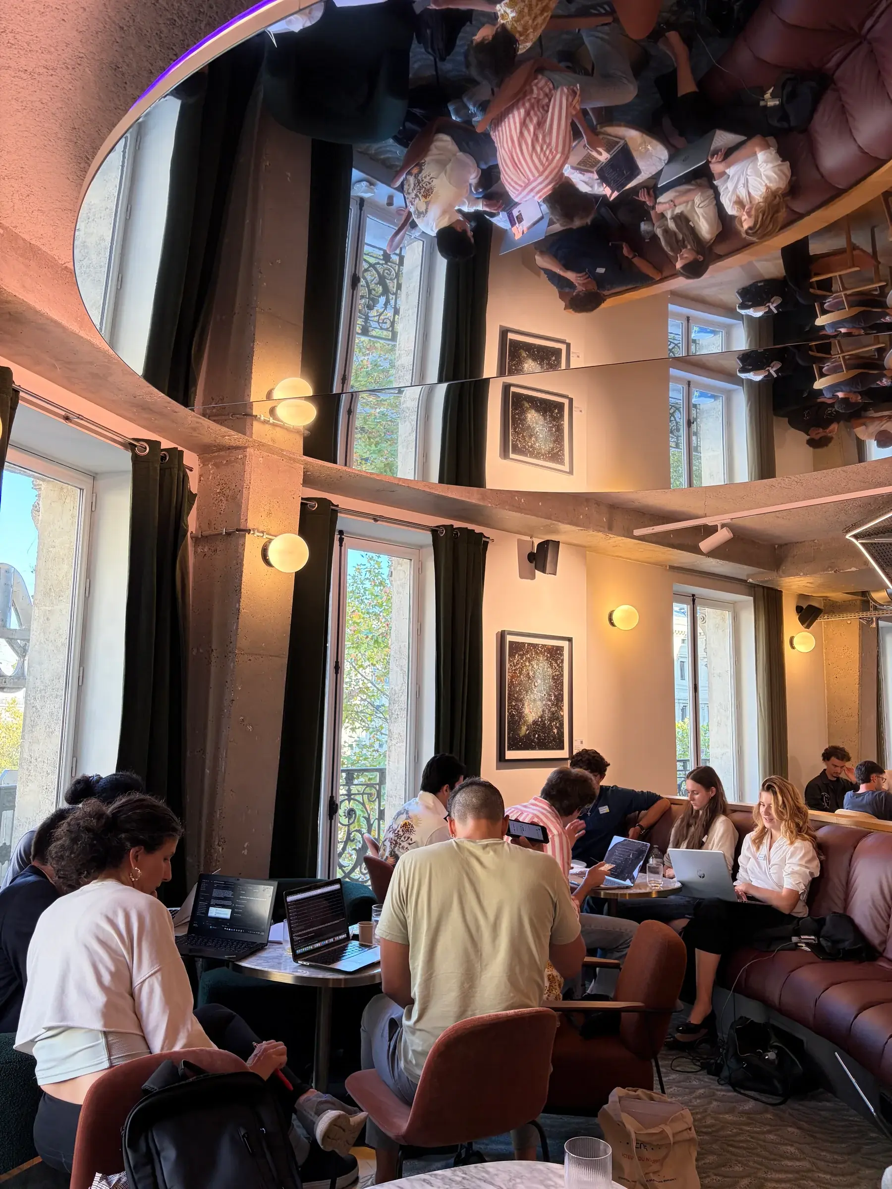 Hackathon participants working on laptops beneath a mirrored ceiling